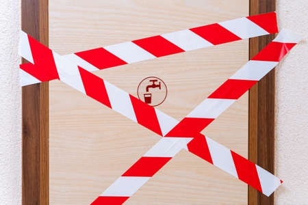 Wooden door with a tap and glass pattern, which is blocked by signal tape. Entrance to the room is prohibited due to an accident or due to some kind of technical malfunctionの写真素材