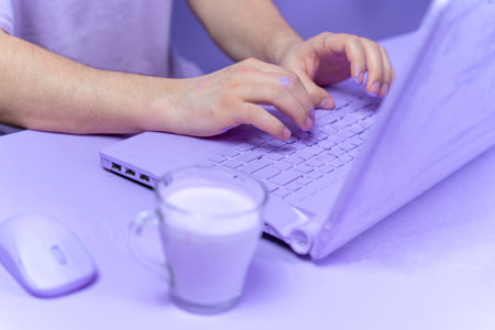 Close-up of hand stained in paint work on laptop, entire interior in one lilac color. Designer, decorator, freelancer, passionate about work, sits at computer in stream, inspired. Workplace monochromeの写真素材