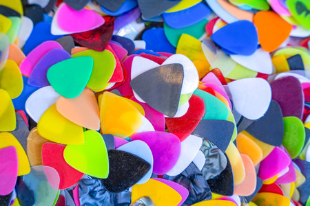 Pile of bright plastic mediator in the storefront of a music store for guitarists. Disposable cheap plectrum for learning to play a musical instrument. Collection of colored picks randomly scatteredの写真素材