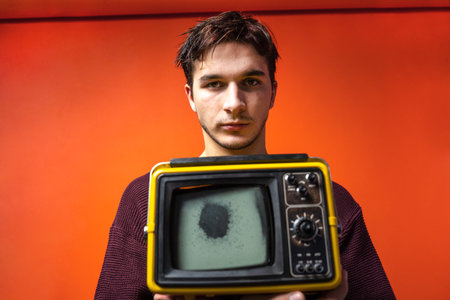 Young man with messy hair marginal look old vintage broken TV zombified passive look on a red background. Activist youth against fake false news TV propaganda. Zombie fake news. Addicted manの写真素材