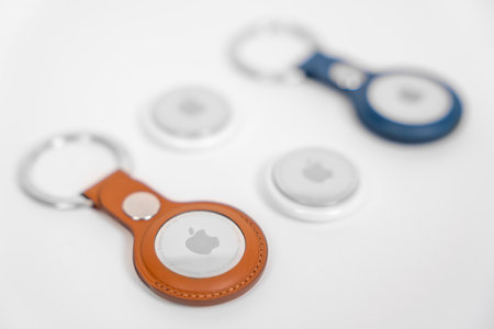 Rostov, Russia - April 04, 2022: Two Apple AirTags lie on a white surface, one in leather key ring...