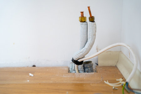 Disconnected plumbing pipes and exposed electrical wires on wooden floor.の写真素材