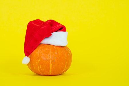 A playful pumpkin wearing a santa hat, set against a vibrant yellow background, blending halloween and christmas themes.の写真素材
