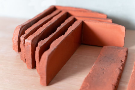 A close-up of red clay bricks neatly stacked and aligned on a wooden surface, showcasing texture and...
