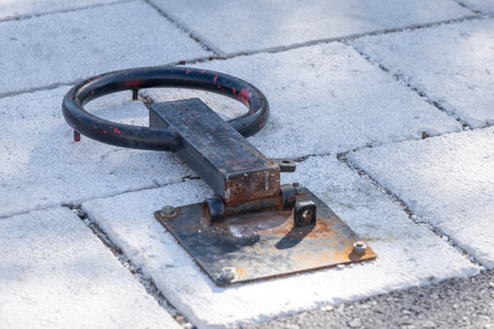 Close-up of a rusty metal ground loop fixed on a concrete pavement, showing signs of wear and age....