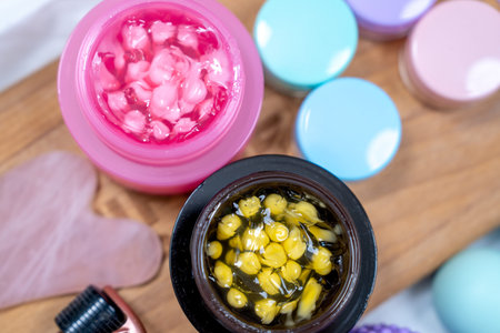 Overhead view of vibrant pink and yellow skincare creams in open jars, surrounded by pastel lids and beauty tools, highlighting self-care and beauty trends.の写真素材