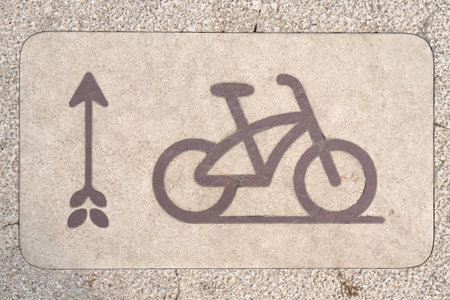 A painted sign showing a bicycle and directional arrow is marked on a concrete sidewalk to indicate a cycling pathの写真素材