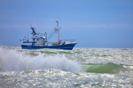 blue fishing boat in the north sea at blue sky and wavesの写真素材