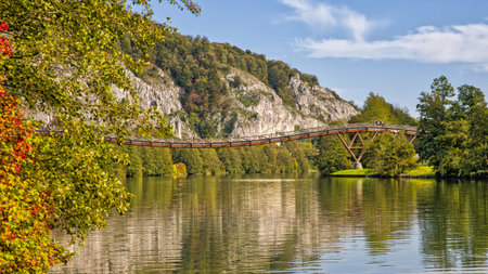 the famous pedestrian wooden bridge tatzlwurm over the rhine-main-danube canal with hikers in sunlight and autumnal treesの写真素材