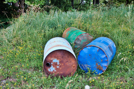 old rusty oil barrels lie on a green meadow with tall grass