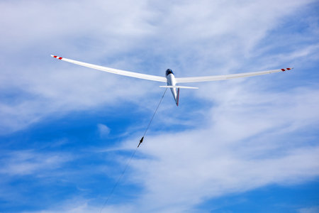 a white glider is pulled up steeply into the sky by a wind in a sunny skyの写真素材