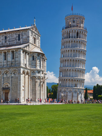leaning pisa tower and baptistery with meadow and blue skyの写真素材