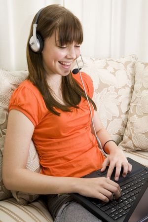 Closeup of a teenager girl sitting on a couch talking with a headset and laptopの写真素材