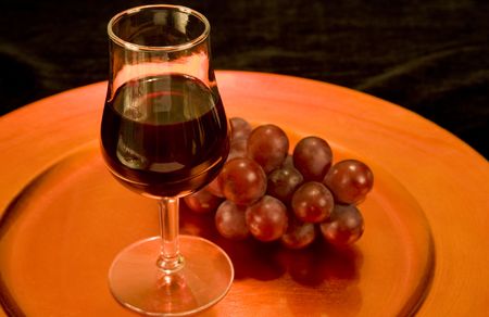 A tasting glass of red wine and grapes on a bronze tray. Black background. の写真素材