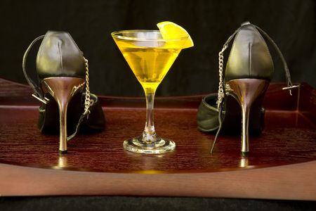 Pair of black high heel shoes and yellow cocktail on a wooden trayの写真素材