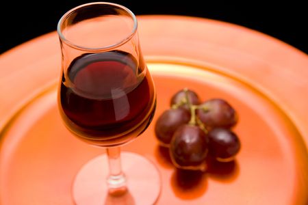 Closeup of a glass of red wine and red grapes on an orange tray. Black backroundの写真素材