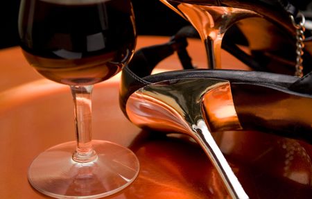 Closeup of a glass of red wine and high heel shoes on an orange tray.の写真素材
