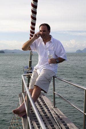 Handsome man on deck of yacht with mobile phone and drinking wineの写真素材