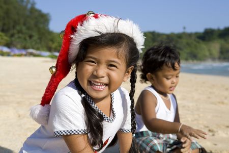 Thai girl wearing a Christmas hat with a boy playing on a beachの写真素材
