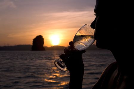 A silhouette of woman having a glass of wine during a beautiful sunset on the oceanの写真素材