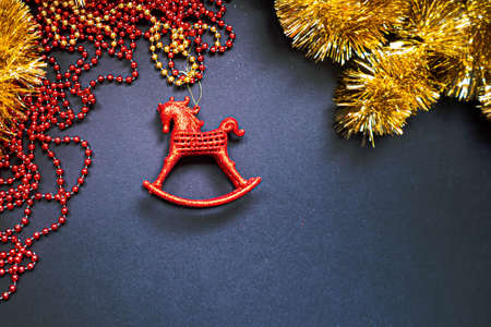 Christmas golden tinsel and red garland on black background. Happy New Year Banner, Merry Christmas. Xmas posters, greeting cards, headers, website. Red horse toy. Space for text. Top viewの写真素材