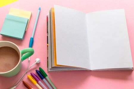 Sketch pad (notebook), multi colored pens, mug with coffee and headphones on the pink background. Stationery in top view design with text space.の写真素材