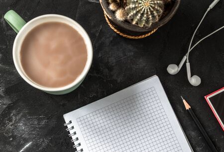 Working place with open notebook and pencil, coffee cup, headphones, music player and cactus on the black desk.の写真素材