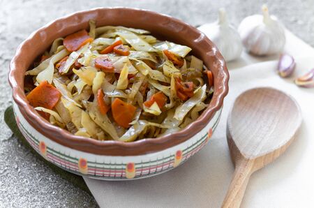 Stewed cabbage in clay bowl and wooden spoon  on the linen napkins on the concrete background. Top view rustic designの写真素材