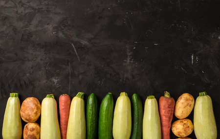 Raw fresh vegetables on the black background in line in top view. Zucchini, carrot, cucumber and potatoの写真素材