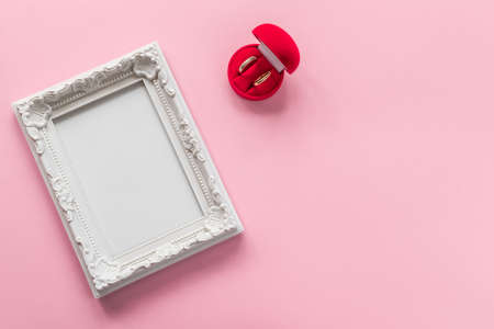 Gold rings in red box and photo frame with empty space on pink background. Wedding / engagement concertの写真素材