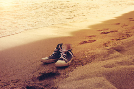 Hipster sneakers in a sea surf on a sand with footprints. Active wild ocean rest, vacation and tourism themeの写真素材