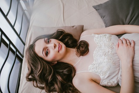 Girl in white dress lying on the bedの写真素材