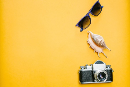 Accessories a traveler on a yellow background with sunglasses, shell and a camera.Top view travel or vacation concept. Summer background.の写真素材