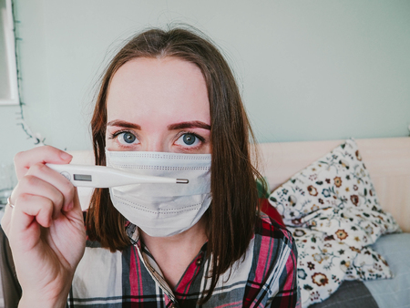 girl in a hospital mask with thermometer in hand