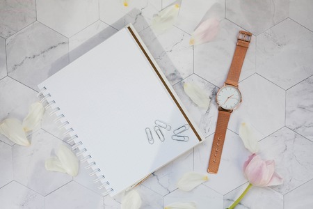 Notepad, paperclip and wrist watch on a marble background.