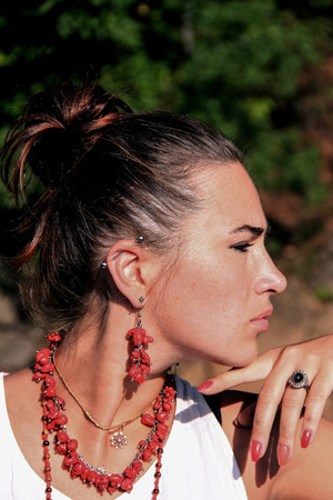 Beautiful young girl posing in profile. Profile of an attractive girl. Girl in red dressing. Red earrings. Portrait of an attractive cute woman on a nature background.の写真素材