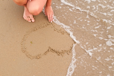 Girl drawing  heart in the sandの写真素材
