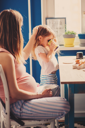 pregnant mother and toddler daughter having breakfast at home, cozy lifestyleの写真素材