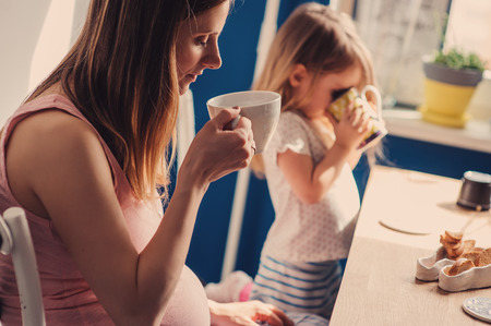 pregnant mother and toddler daughter having breakfast at home, cozy lifestyleの写真素材