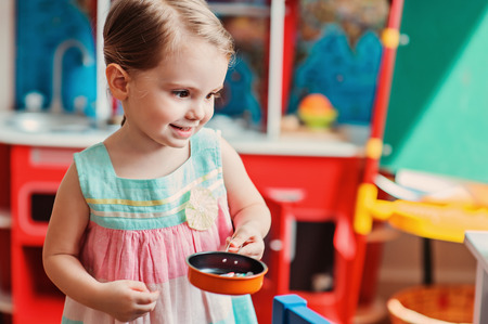 happy toddler girl playing with toy kitchen at homeの写真素材