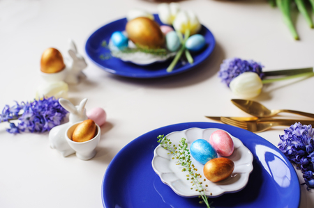 easter holiday festive dining table with golden metallic cutlery and eggs, hyacinth and tulip...