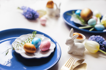 easter holiday festive dining table with golden metallic cutlery and eggs, hyacinth and tulip bouquet, blue and white plates. Celebration conceptの写真素材
