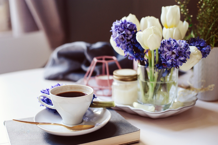 spring morning at home with cup of coffee, book and flowers on white table. Seasonal decoration, cozy living, hygge conceptの写真素材