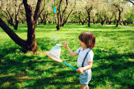 happy 3 years old child boy catching butterflies with net on the walk in sunny garden or park. Spring and summer outdoor activities, happy childhood concept.の写真素材