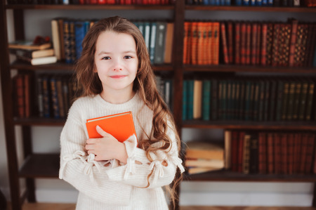 happy smart schoolgirl reading books in library or at home. Kids early learning and education concept.の写真素材