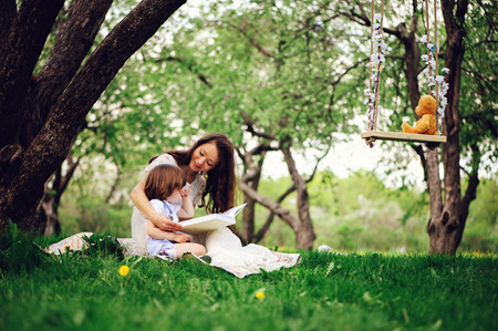 loving mother reading book to toddler son outdoor on picnic in spring or summer park. Happy family and mothers day conceptの写真素材