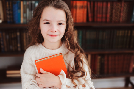 happy smart schoolgirl reading books in library or at home. Kids early learning and education concept.の写真素材