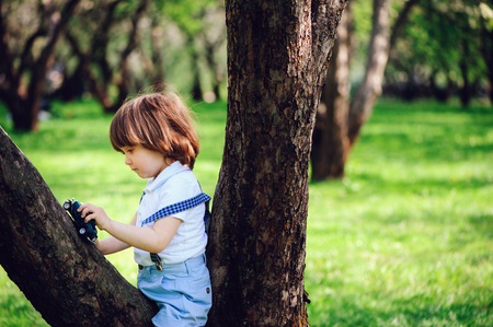 cute toddler child boy with long hair in stylish outfit playing with toy car on the walk in summer or sping garden, sitting on big treeの写真素材