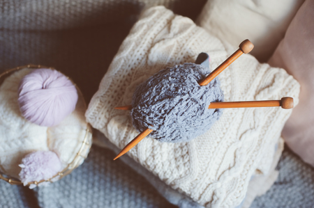 Grey and pink Yarn ball with knitting needles in metallic basket with knitted sweaters on background. Hobby, cozy homely weekend and hugge concept.の写真素材