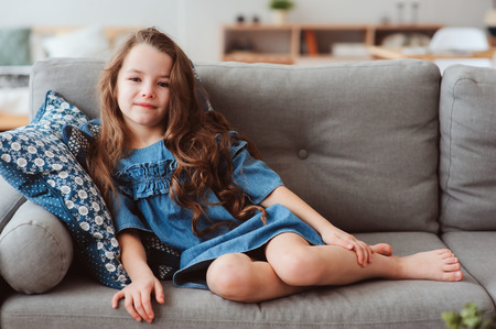 cute happy 5 years old child girl relaxing alone at home on cozy couchの写真素材